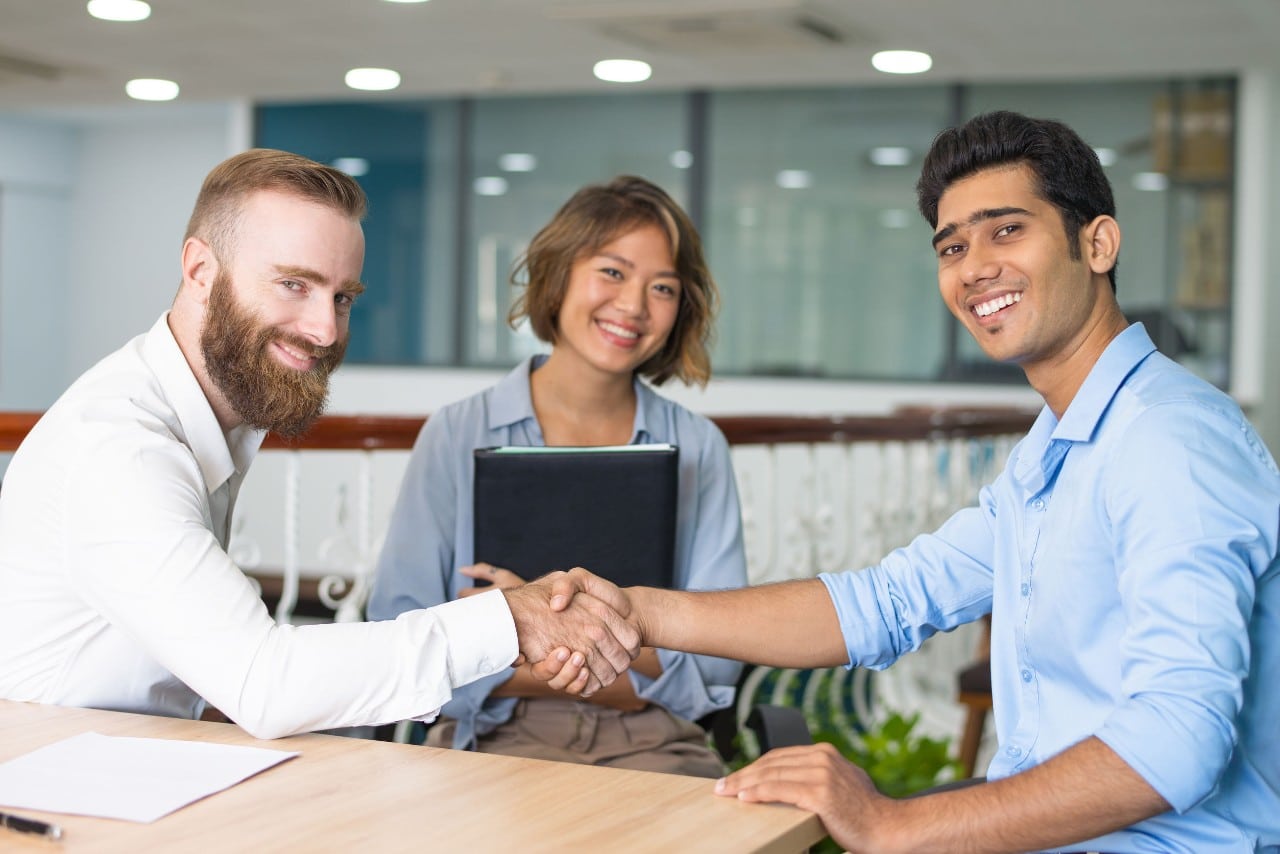 three office workers, two shake hands; concept: ai complements ats to find great hires