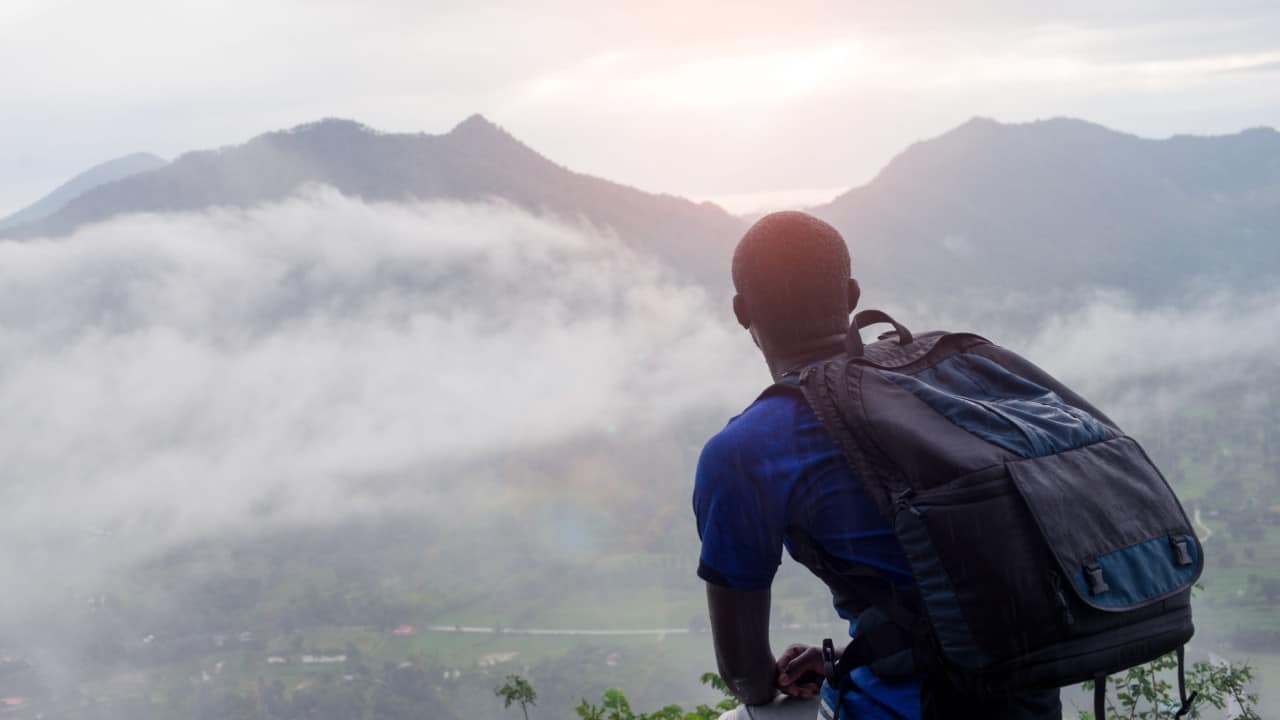 vacationer with backpack looks out on beautiful mountains; unlimited paid time off policy (PTO) concept