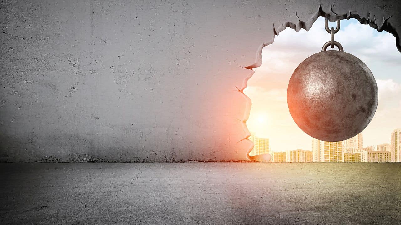 A black wrecking ball hanging inside the opening in a concrete wall showing city landscape; hire for skills concept