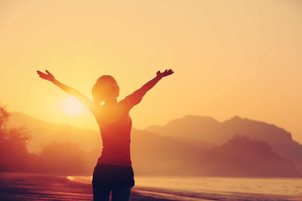 woman on beach with arms raised at sunrise; oil and gas industry hiring concept