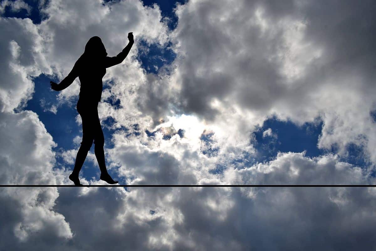 silhouette of a woman balancing on a highwire in the sky; motherhood penalty concept