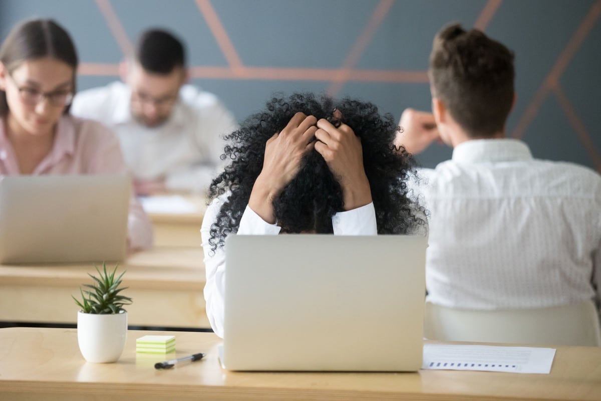 Frustrated woman feeling despair sitting in shared office with laptop; imposter syndrome concept