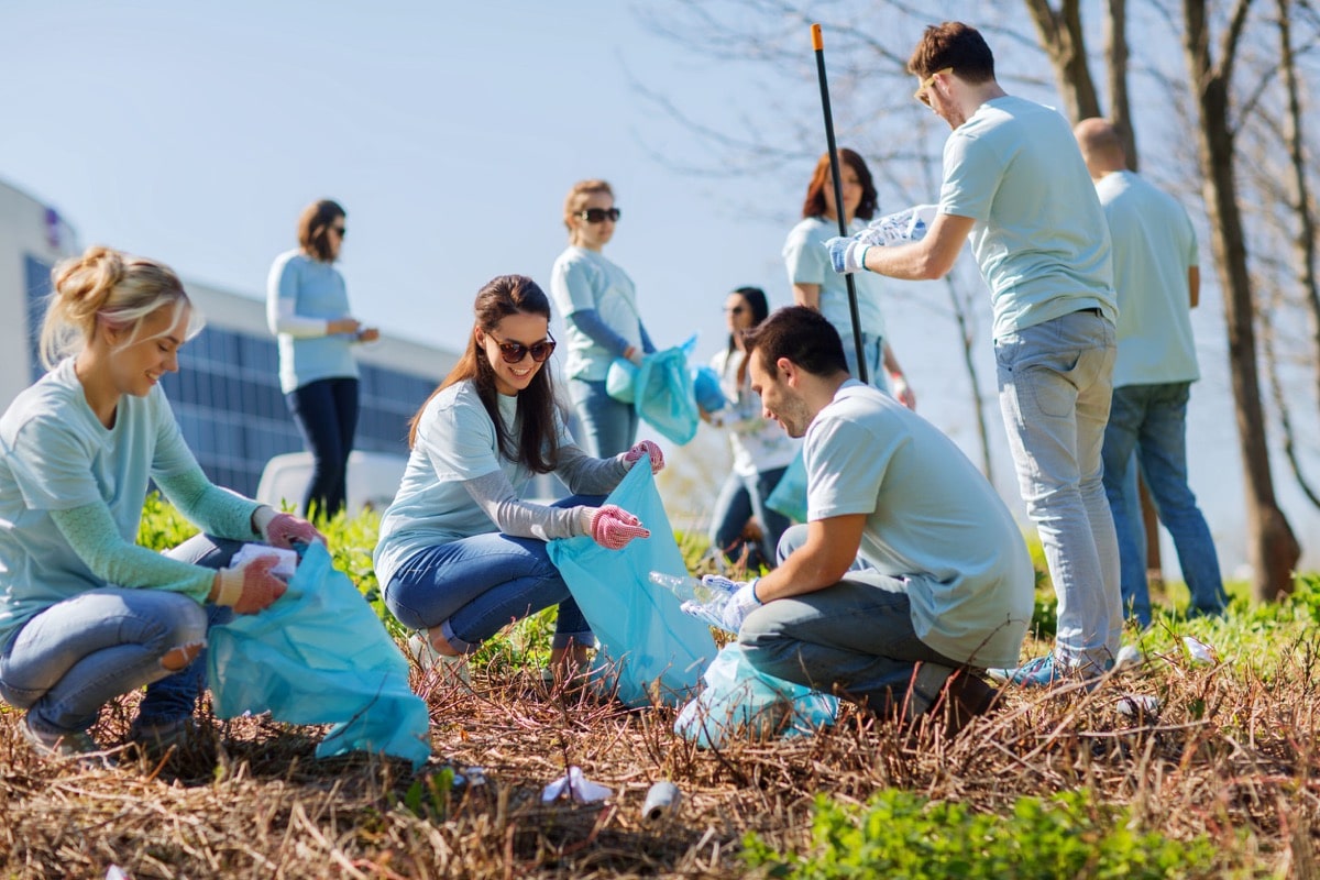 group of happy volunteers with garbage bags cleaning area in park; community involvement concept