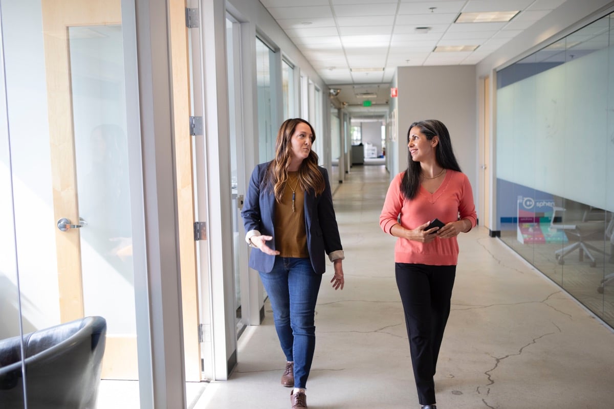 two businesswomen meet while walking through a light-filled hallway; global talent intelligence concept