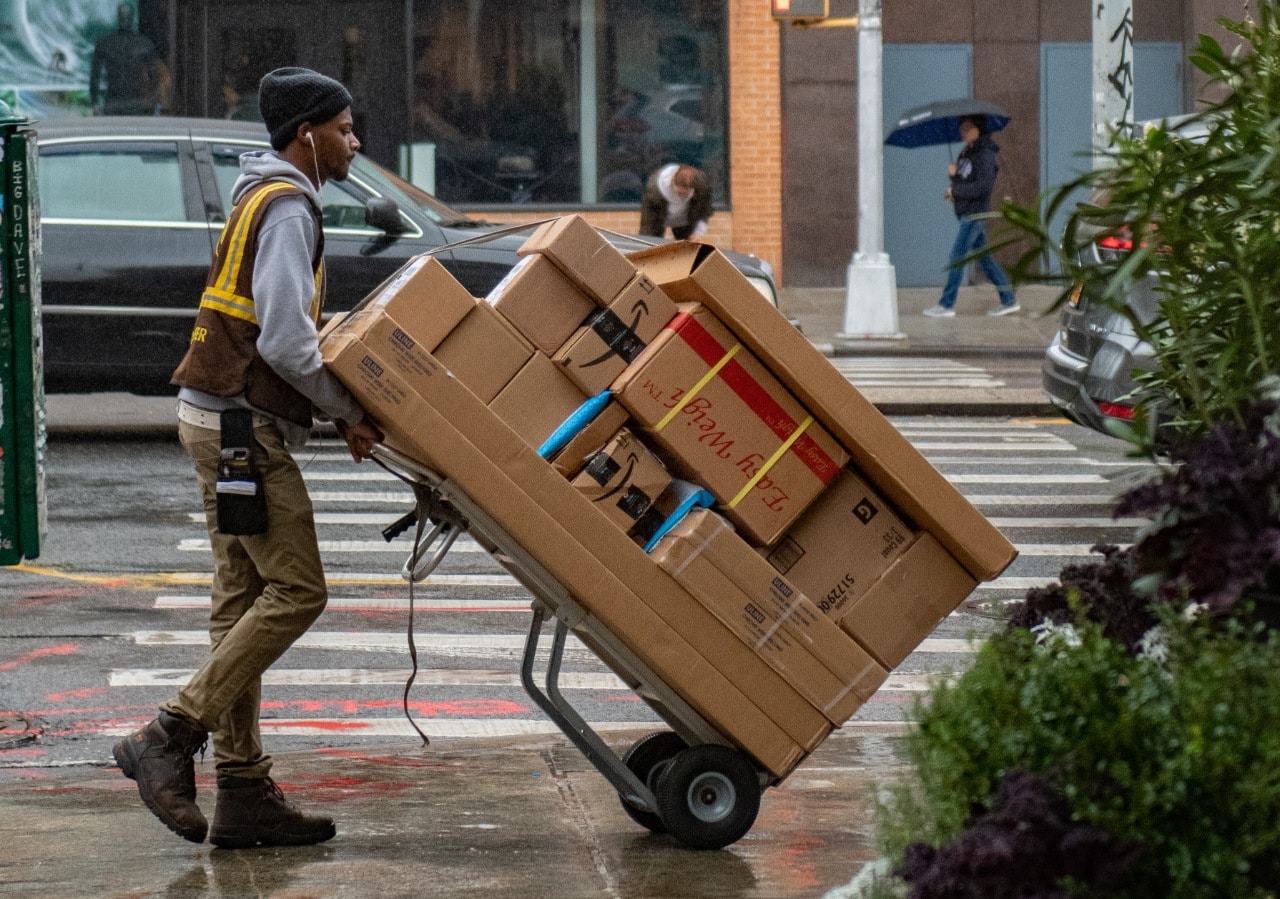 a deliveryperson pushing a dolly overloaded with packages in the rain; DEI in logistics concept