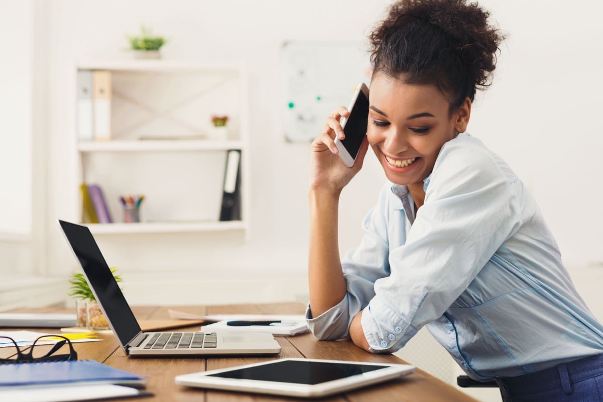 Young female manager consulting on phone, using laptop at work place; future of work concept