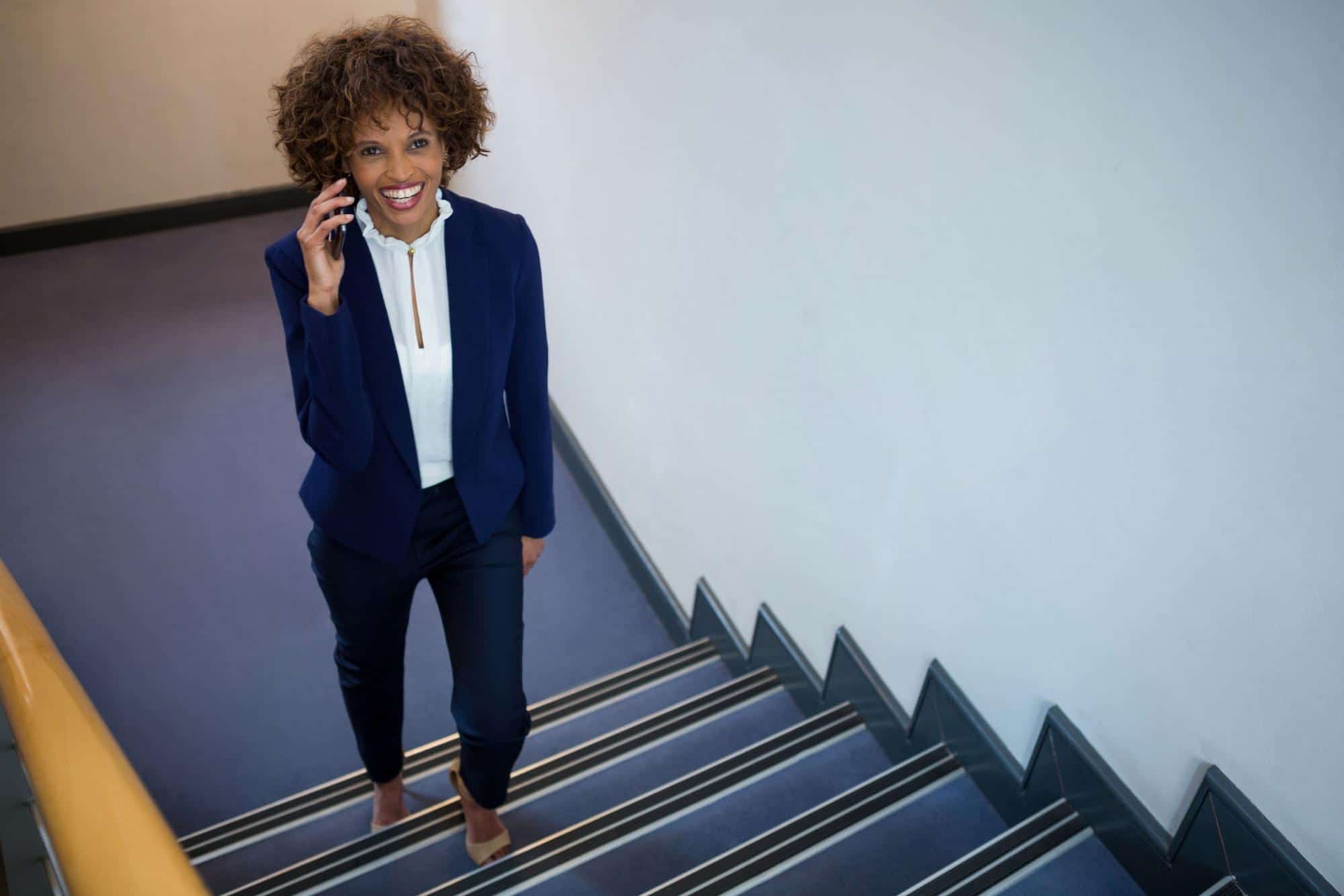 businesswoman on cellphone walking up stairs; job-hopping job market concept