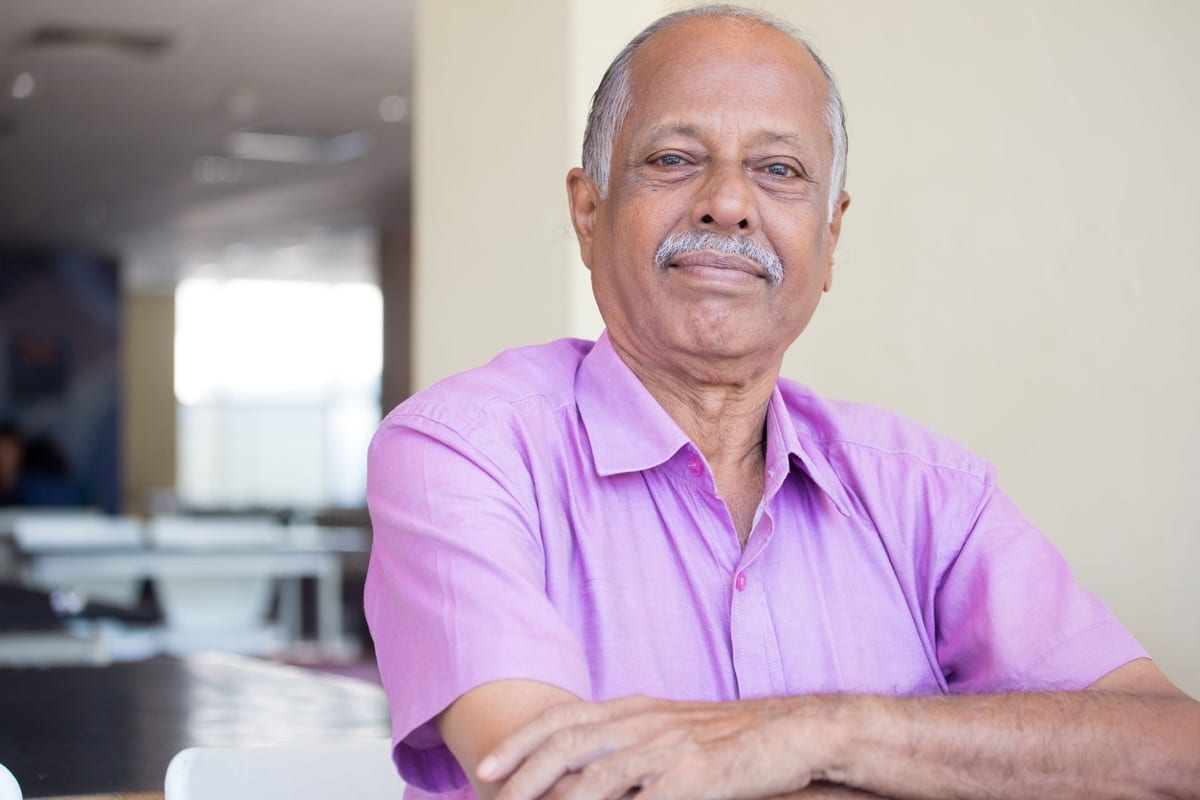 portrait of elderly gentleman arms crossed, in pink shirt smiling; workplace discrimination concept