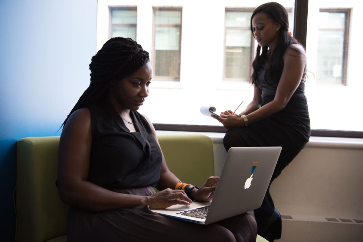 Two businesswomen working on a laptop and using a sketchpad; retaining tech talent concept