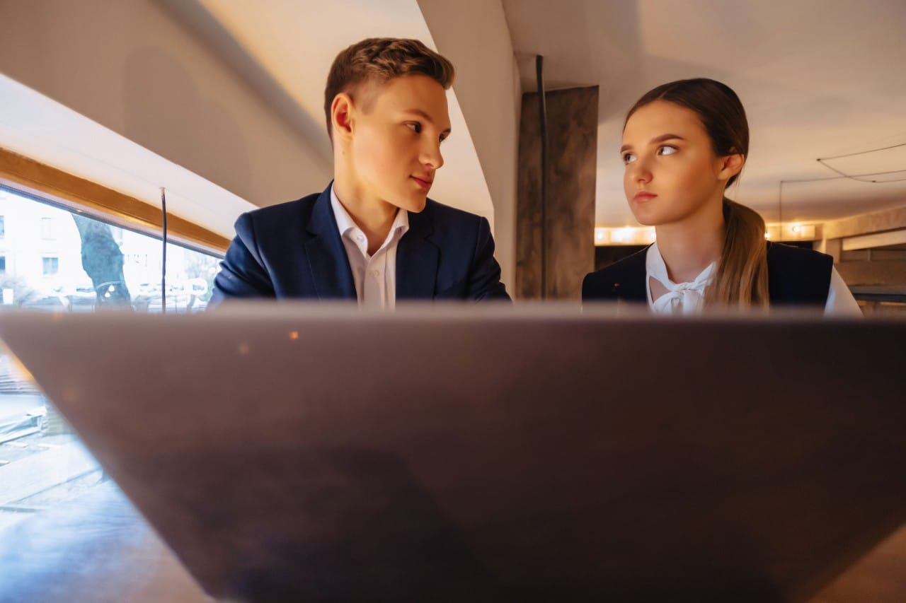 Two young workers share a laptop and appear dissatisfied; retention strategies concept