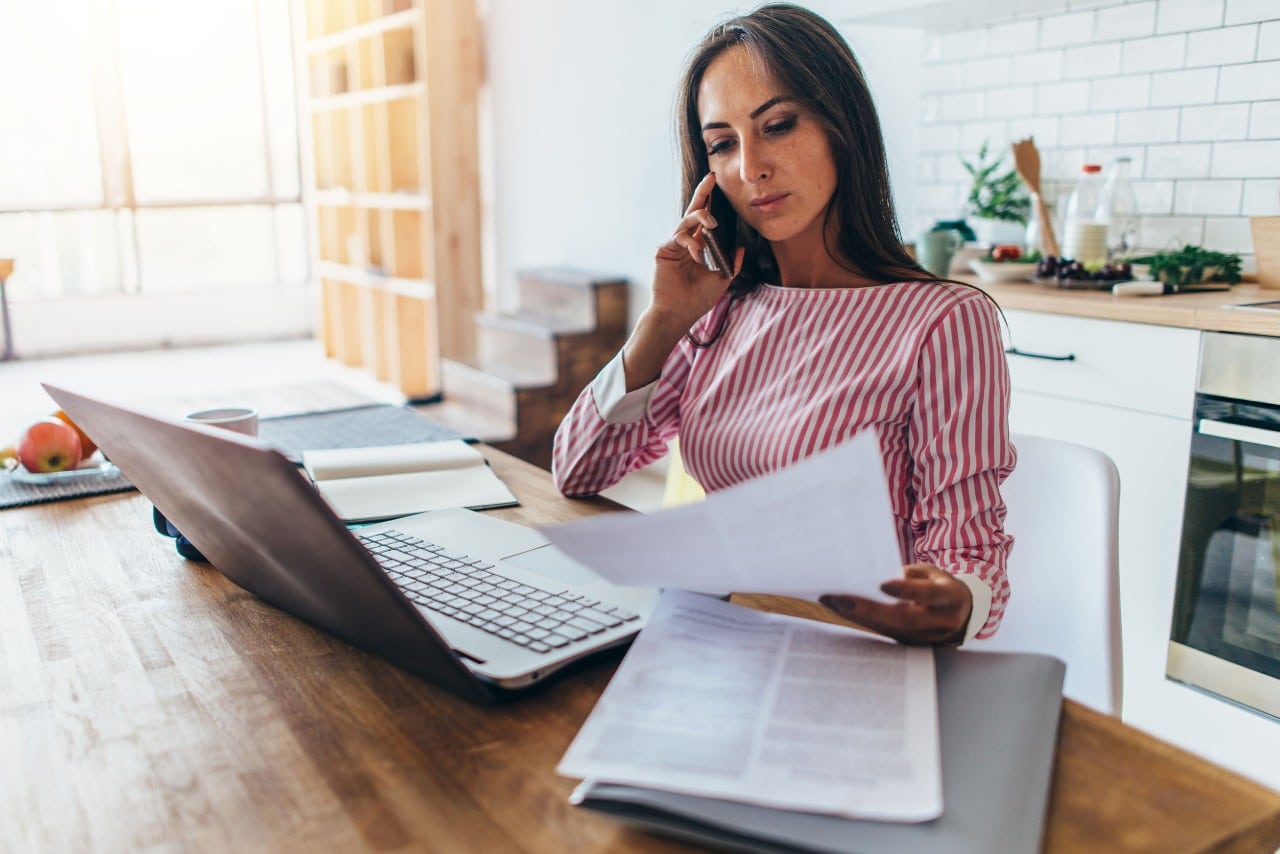 busy worker with laptop, many papers, smartphone working from home at kitchen table; hiring tech and talent pipeline concept
