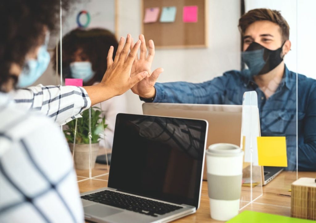 two office workers in masks at laptops; how the pandemic changed Human Resources concept