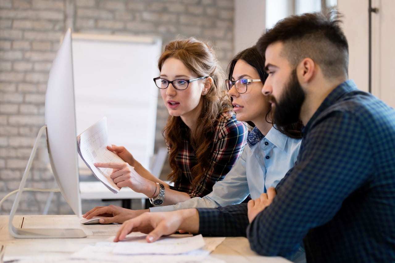 three coworkers crowded around a computer screen working together; Recruitment operations concept