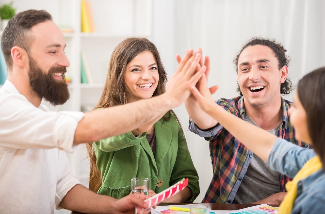 four young hip employees at a conference room table give each other a high-five; contingent workers concept