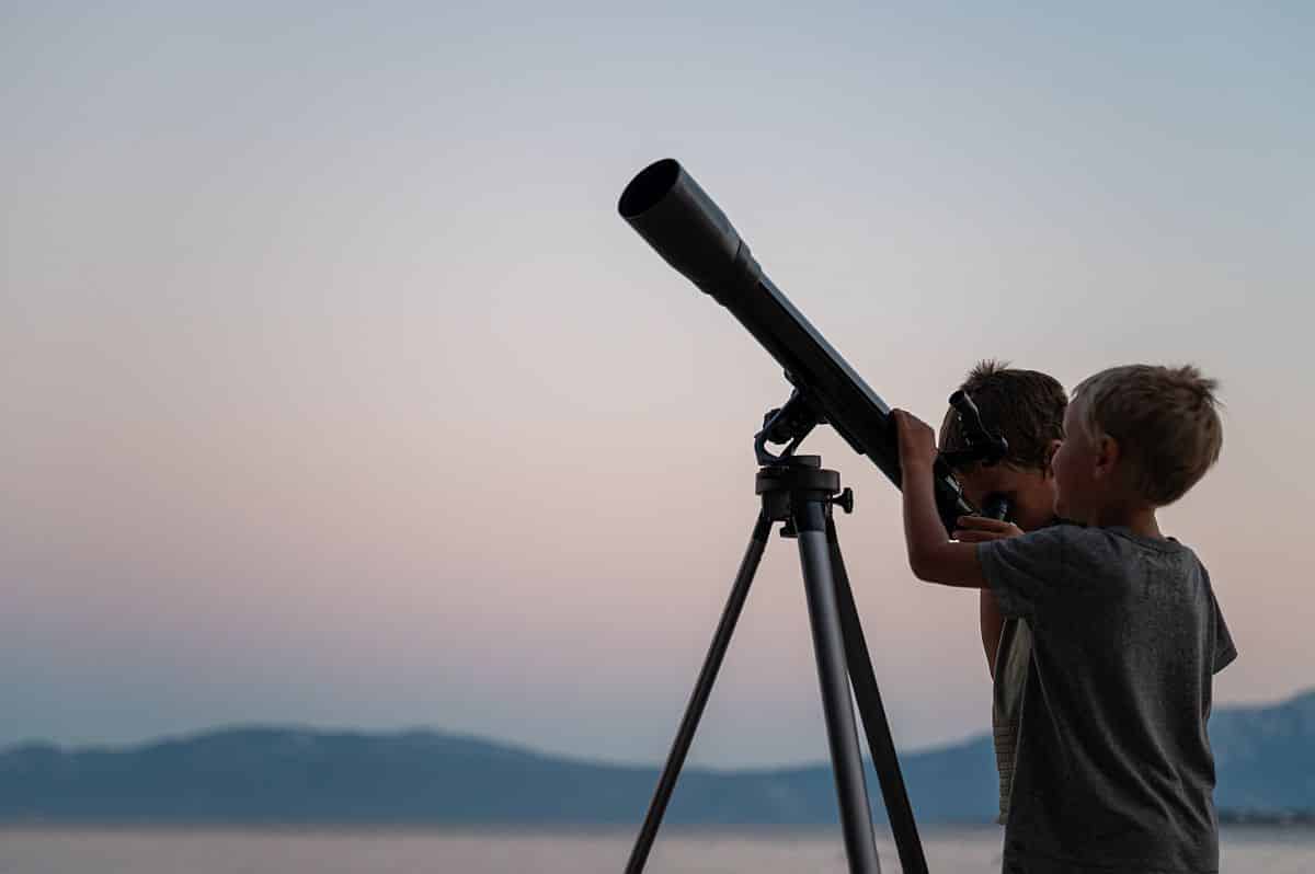 Two brothers, toddler boys, looking at the stars using a telescope by the sea on a beautiful summer night.