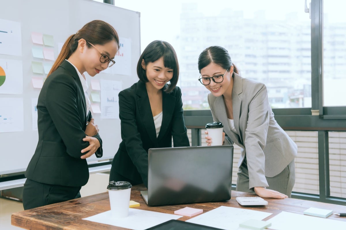 happy pretty office workers having teamwork meeting and standing in office looking at laptop computer; talent crisis concept