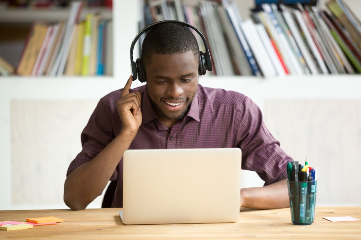 Smiling office worker in headphones looking at laptop screen; adapt your hiring concept