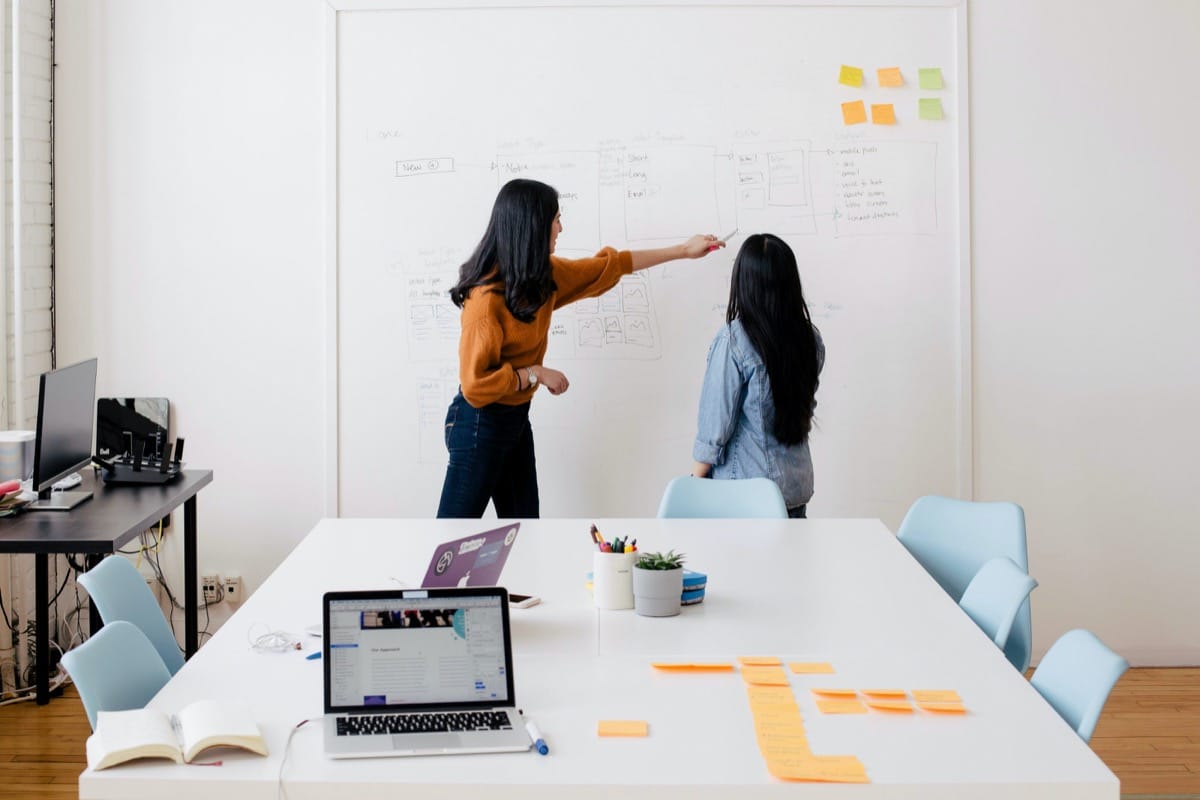 Two business women brainstorm on a whitboard; Change the World list concept