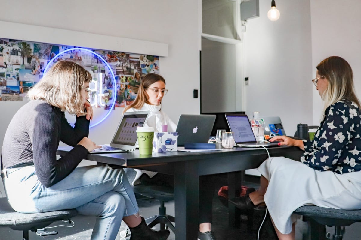 three young creative office workers on laptops at a cluttered desk; retaining tech talent concept