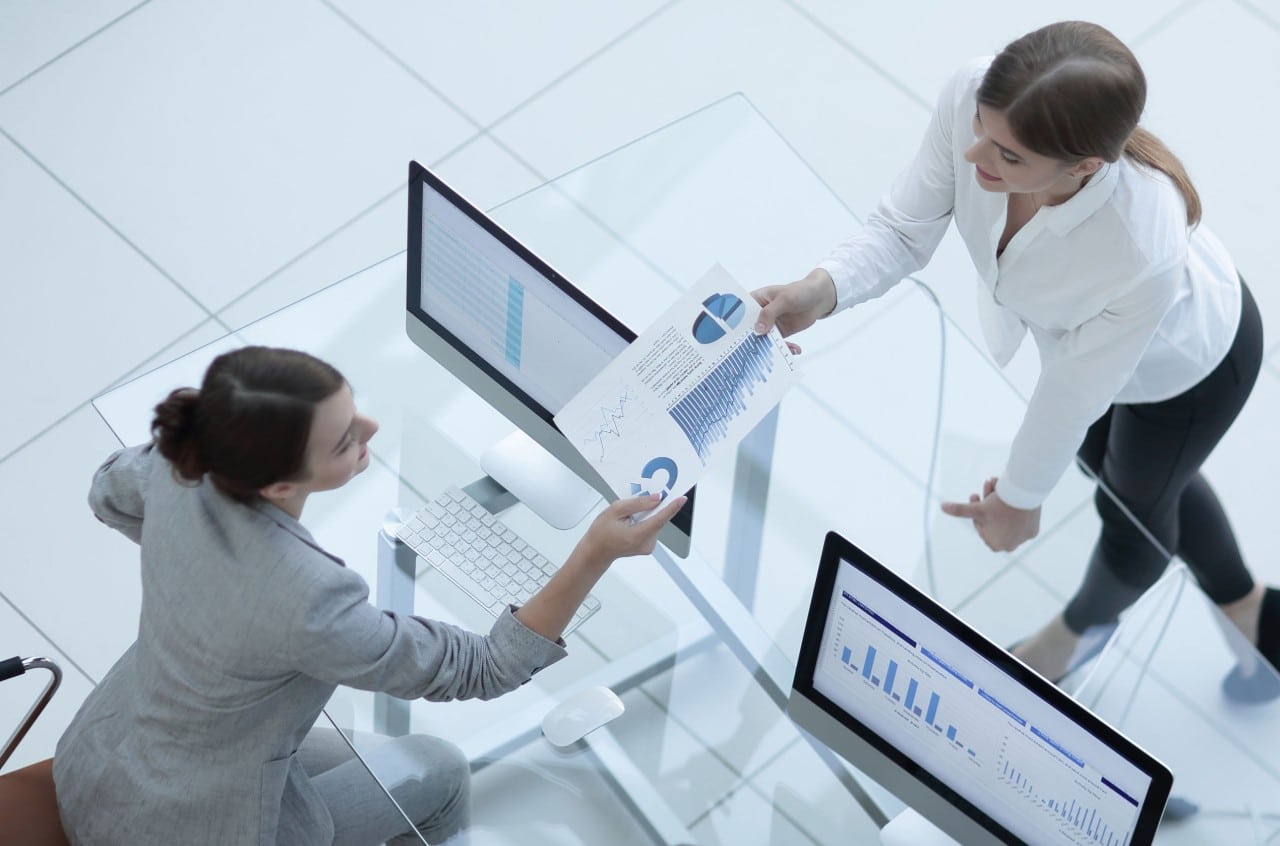 A businesswoman in a very modern office give a sheet of paper with a pie chart on it to a coworker; retention strategies concept