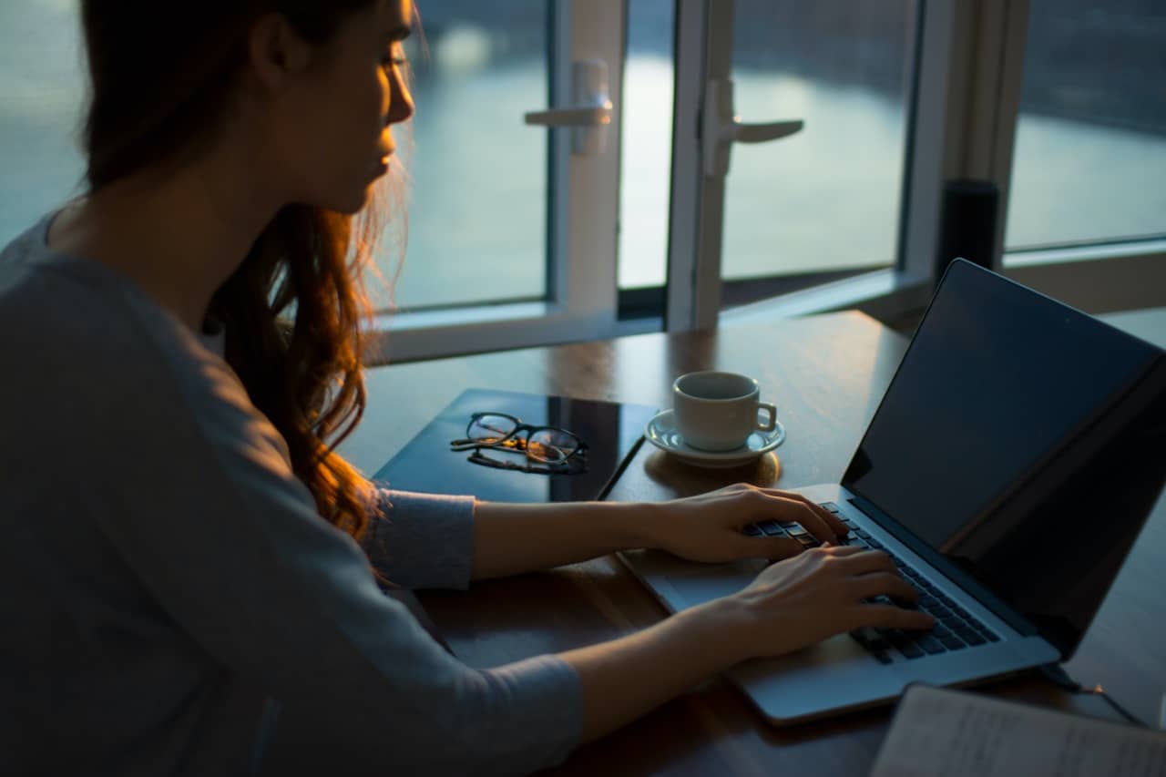 woman works from home at a laptop as the sun sets; Talent Management, Finance and COVID concept