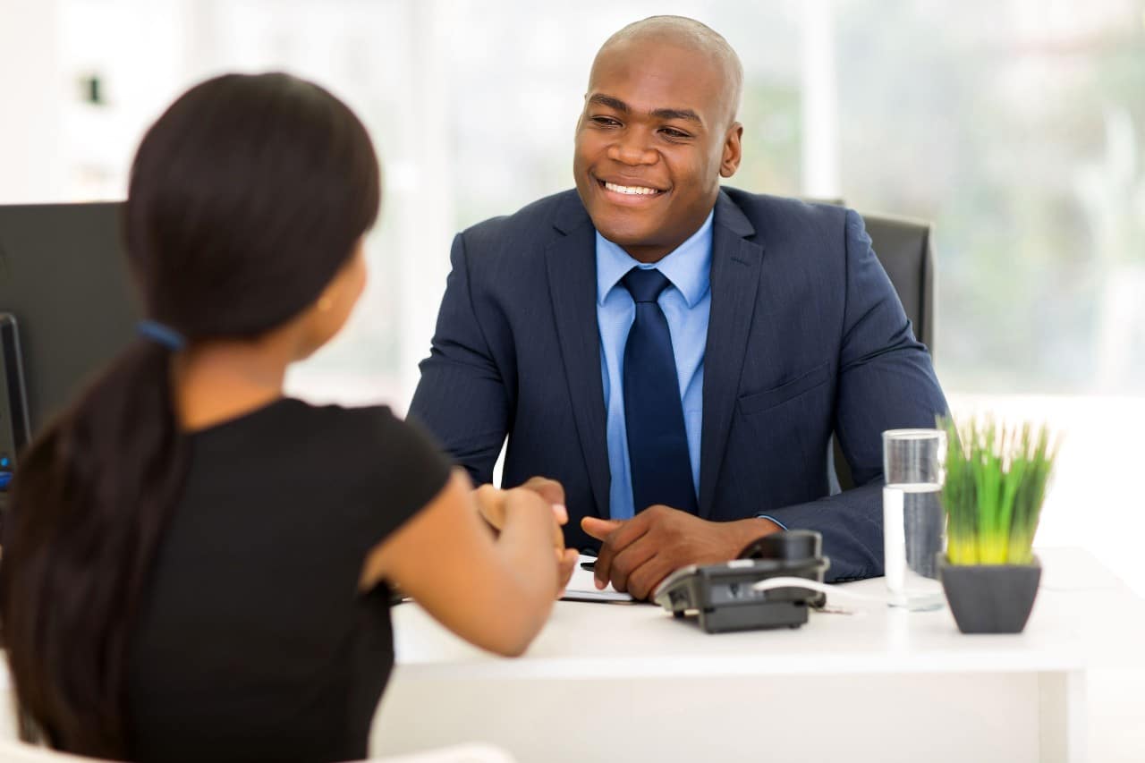 in person job interview, well dress office workers shake hands across a modern desk; hiring tech and talent pipeline concept