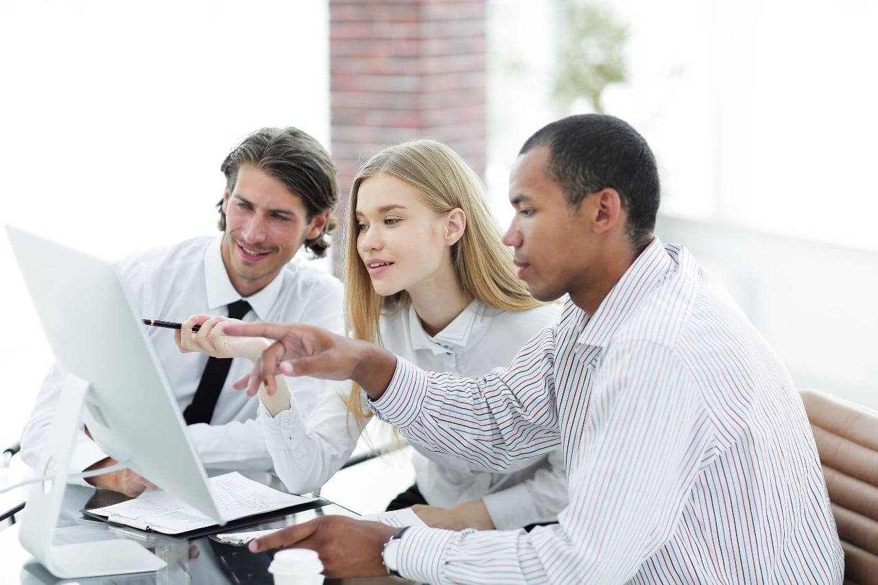 three hip young office employees collaborate at a single desktop computer; workforce planning concept