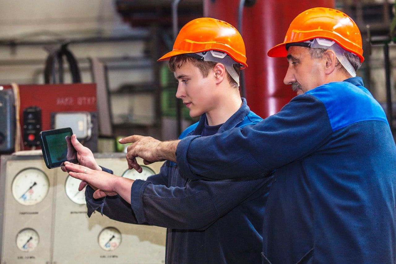 an older and a young worker, both in hardhats use a tablet together; internal talent shifts concept